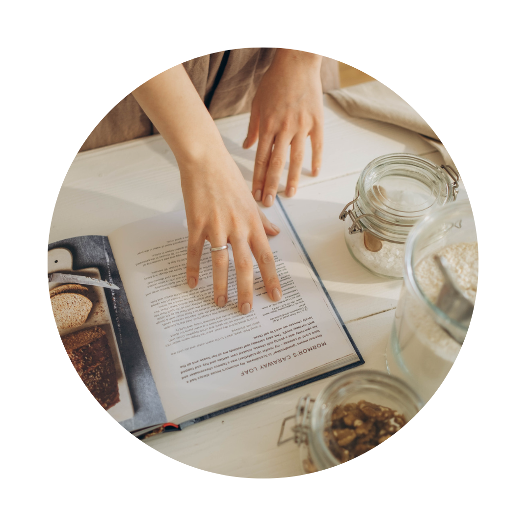 Hand with ring touching cookbook with jars filled with ingredients on the table